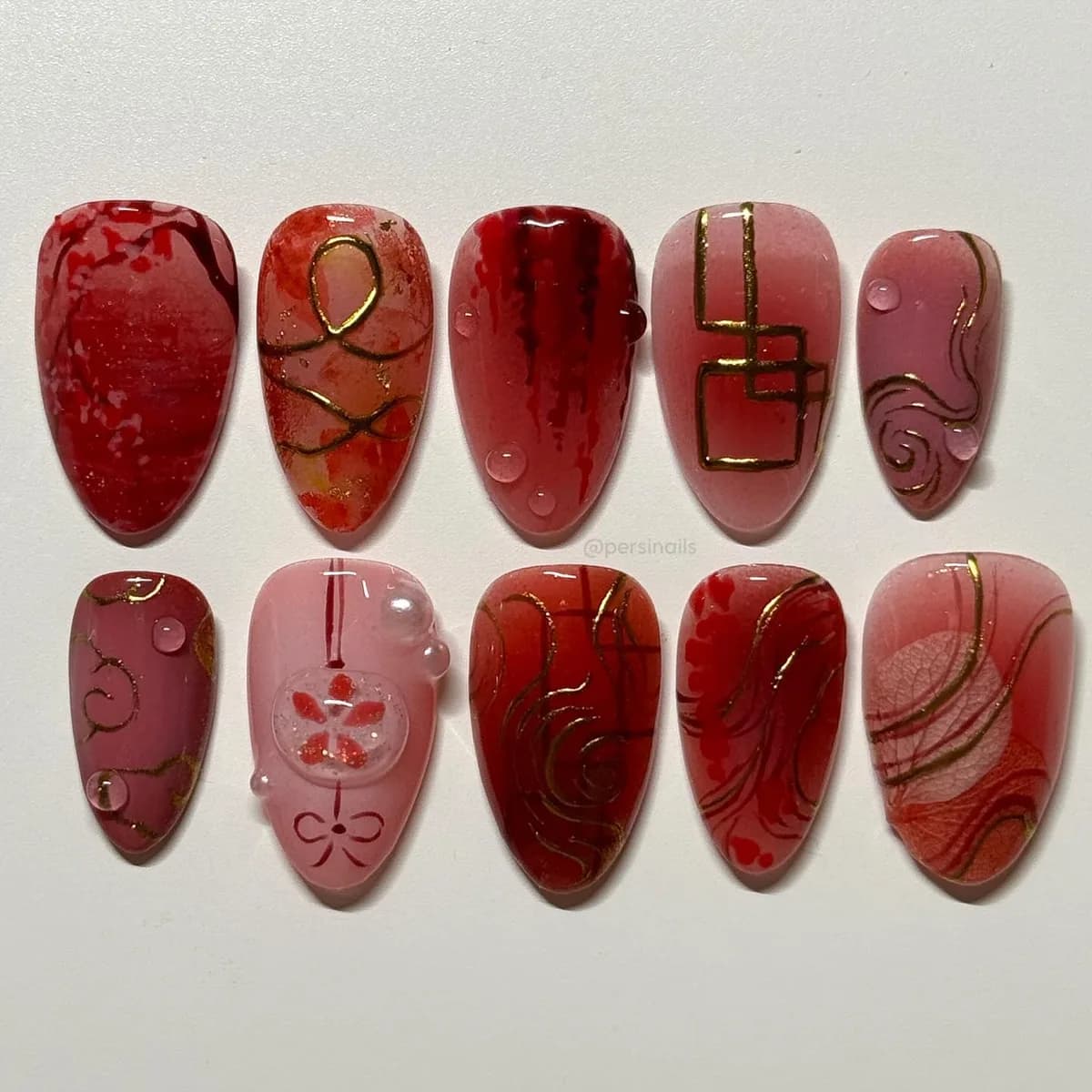 Ten press-on nails in layered translucent red under a wet-look gloss, drawn over with fine gold line work.