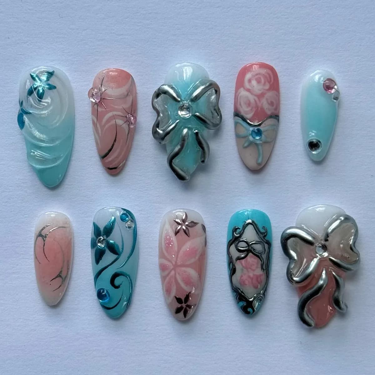 Ten press-on nails in pale blush and mint under a glazed finish, with sculpted silver bows, piped roses and set crystals.